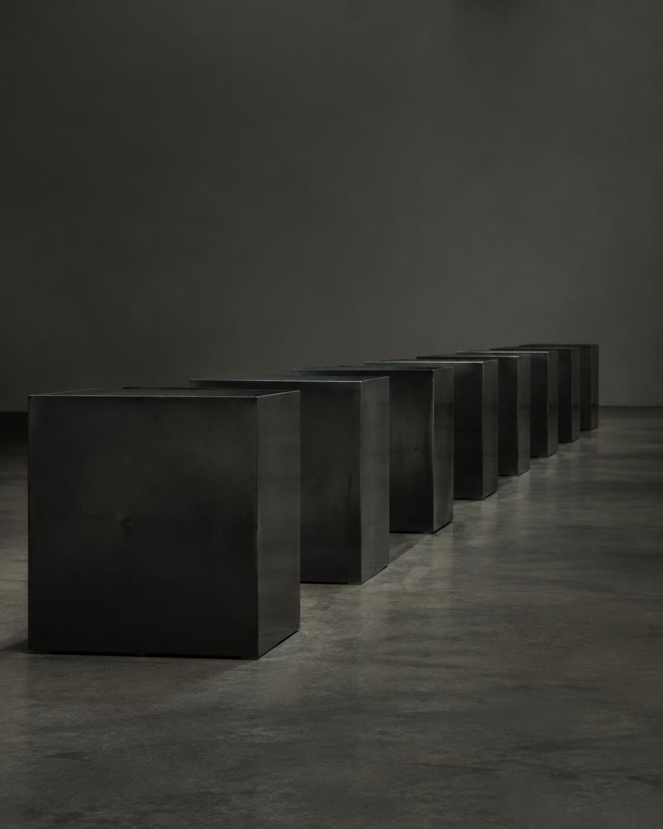 Row of identical dark steel boxes in an empty gallery