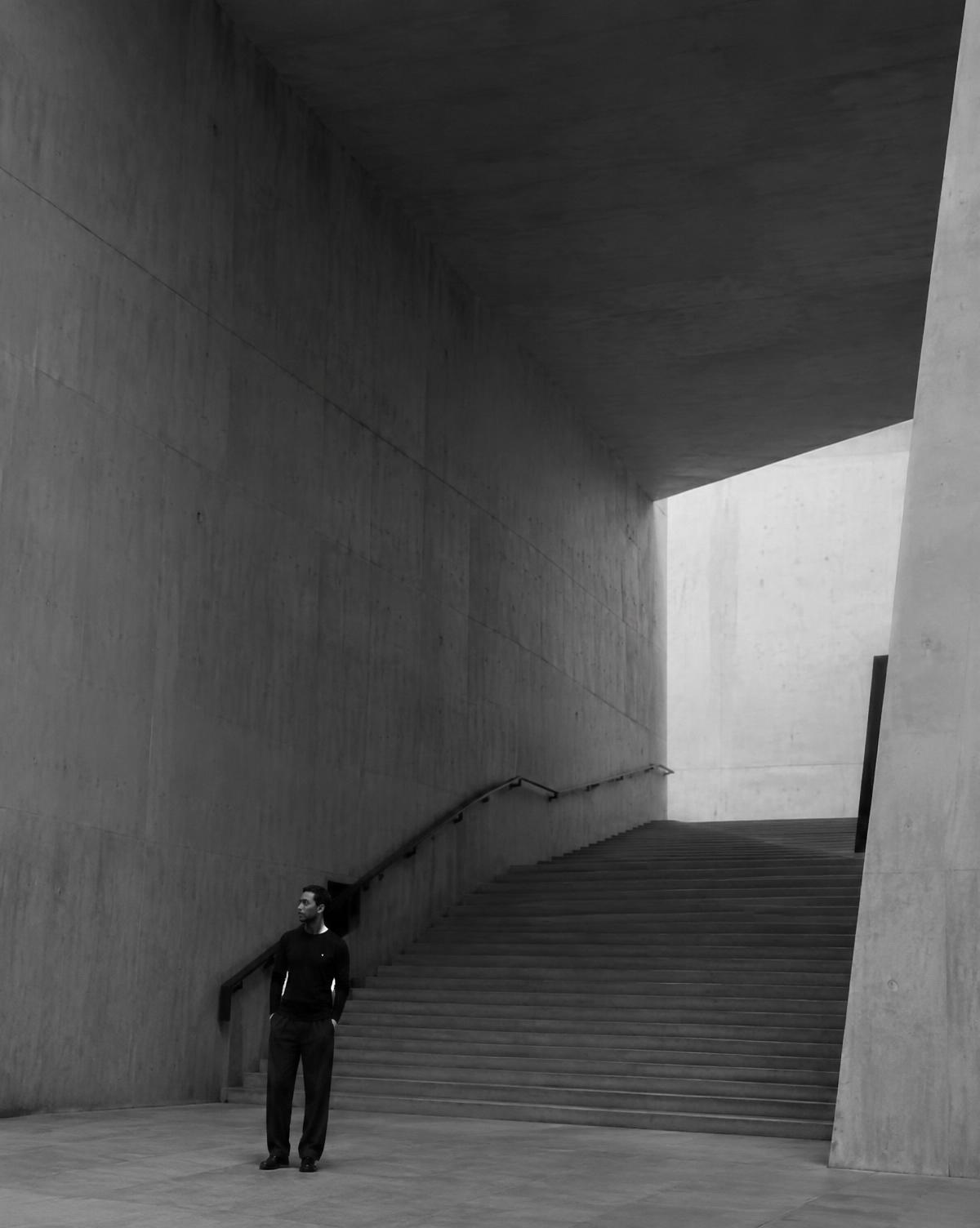Man in black standing in a monumental concrete stairwell