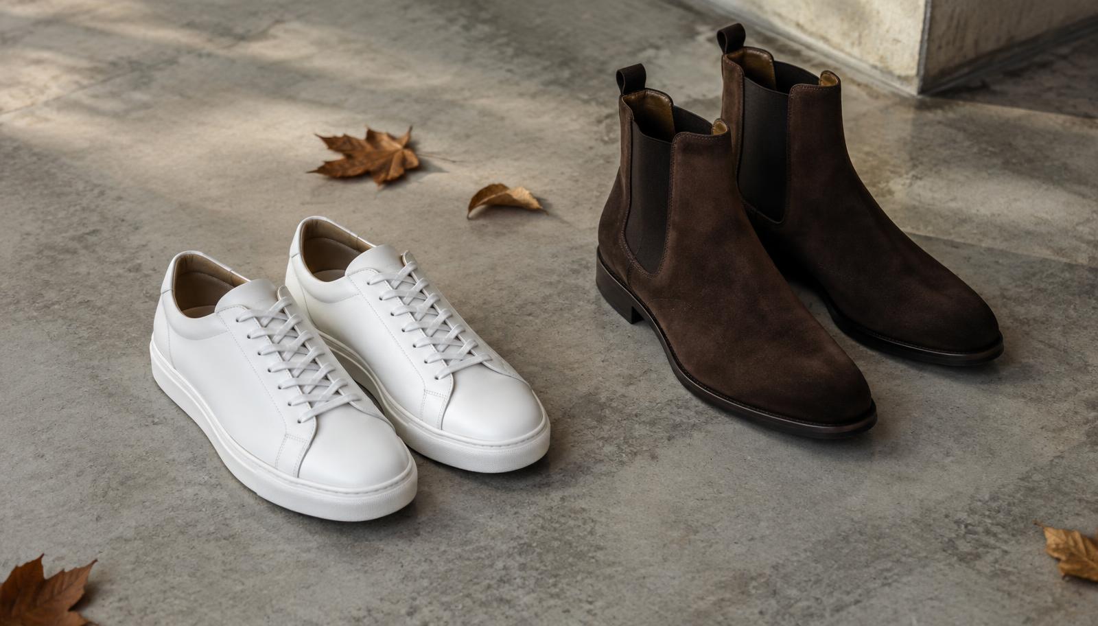 Minimal white leather trainers and brown suede chelsea boots on concrete with autumn leaves