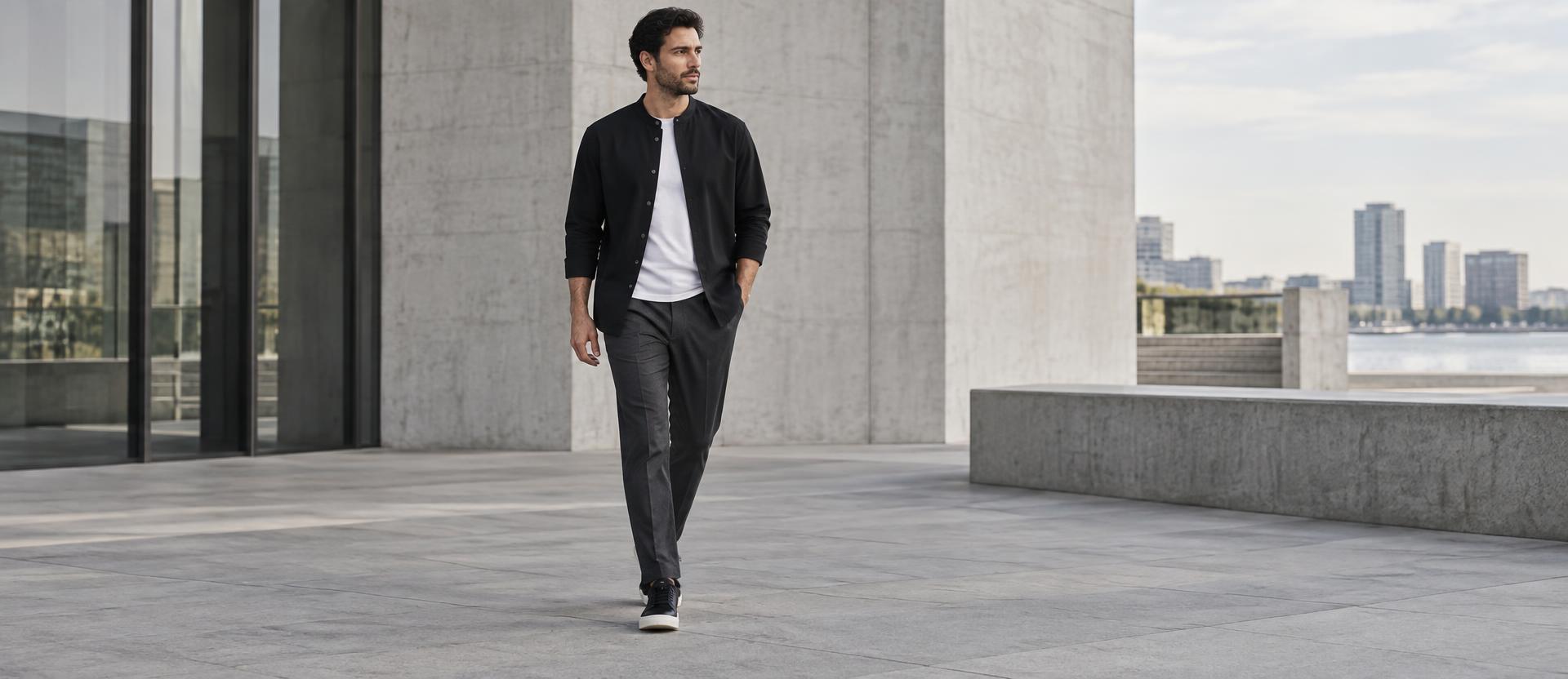 A man in a black shirt, white t-shirt and charcoal trousers walking through a minimal city space