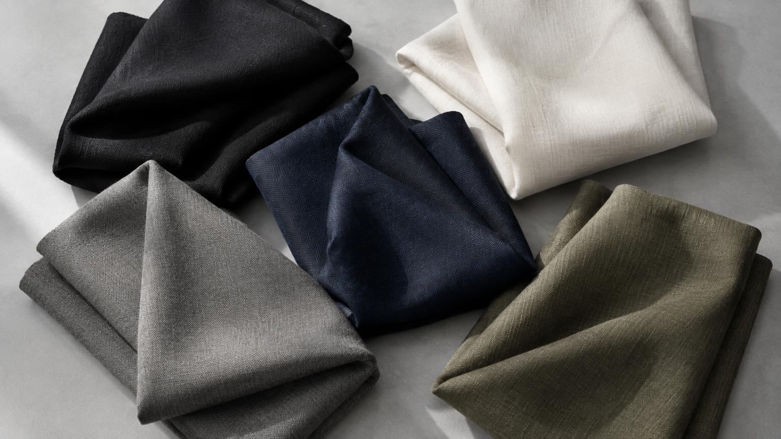 Tissus pliés noirs, blancs, bleu marine, gris et olive.