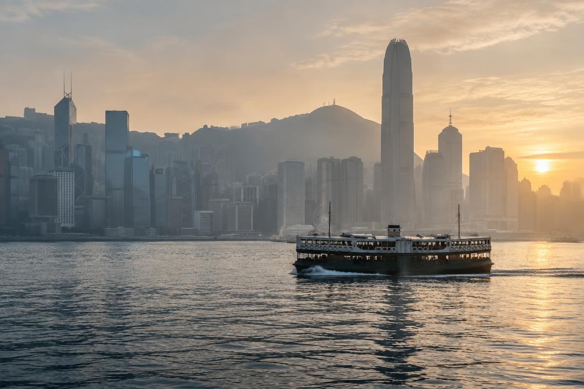 A Star Ferry crossing Victoria Harbour at dawn with the Hong Kong Island skyline behind