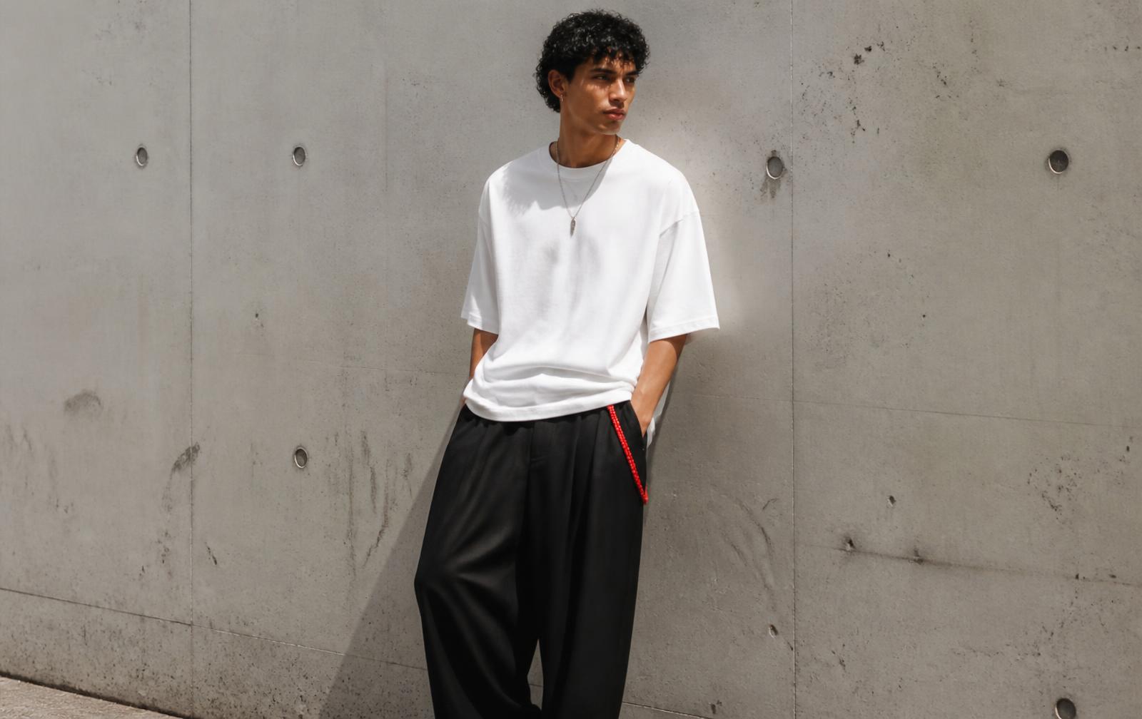Model in an oversized white tee and loose black trousers against a concrete wall